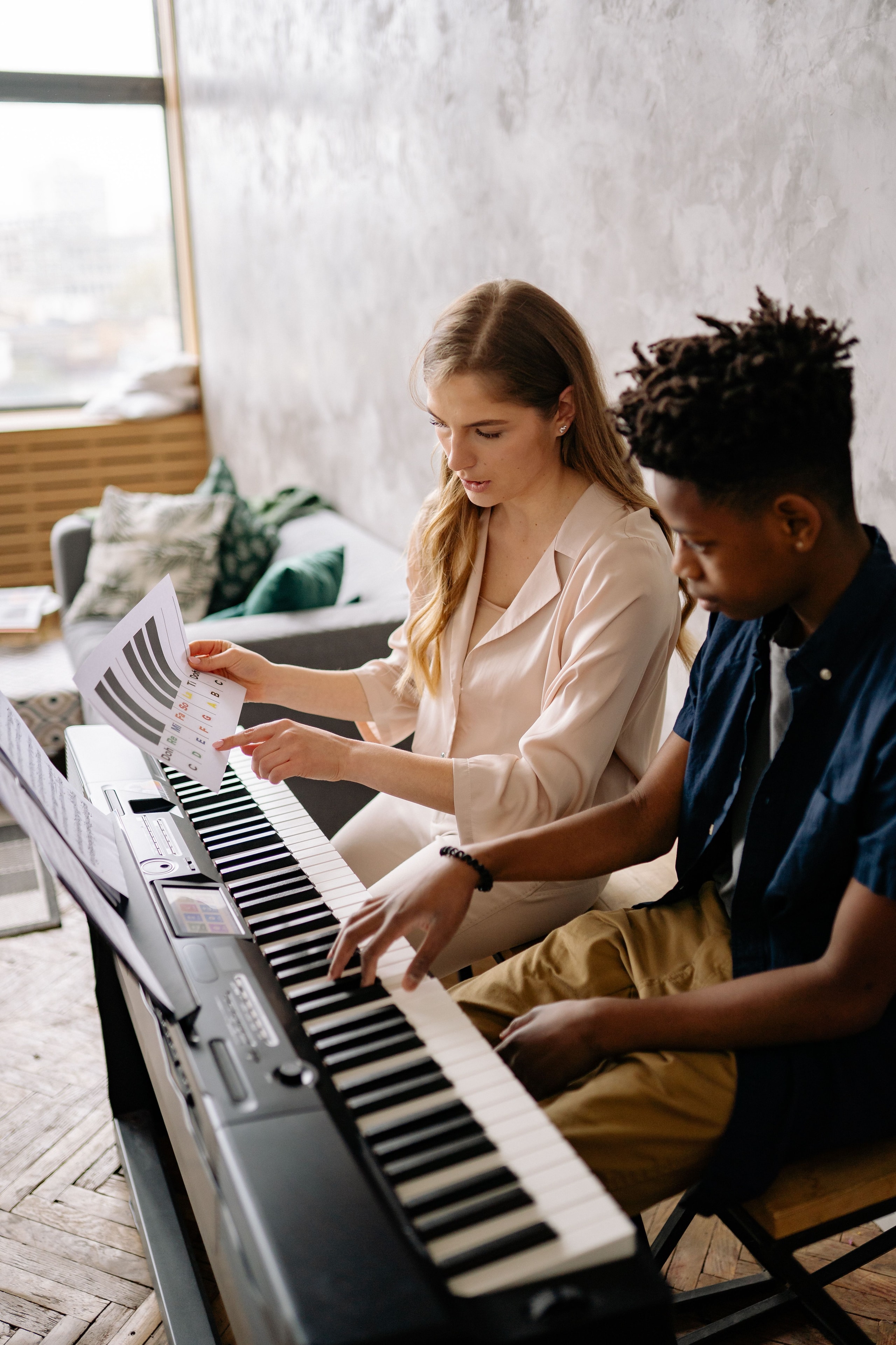 Adult and teen at a keyboard together, sharing sheet music during a piano session
