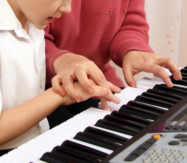 Adult guiding a child's hands at a keyboard, showing hands-on support during a piano session